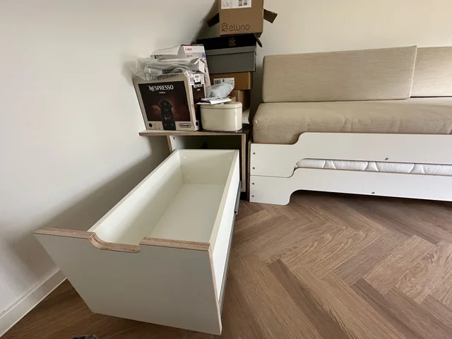 Geöffneter Stauraumauszug auf Rollen neben dem Bett